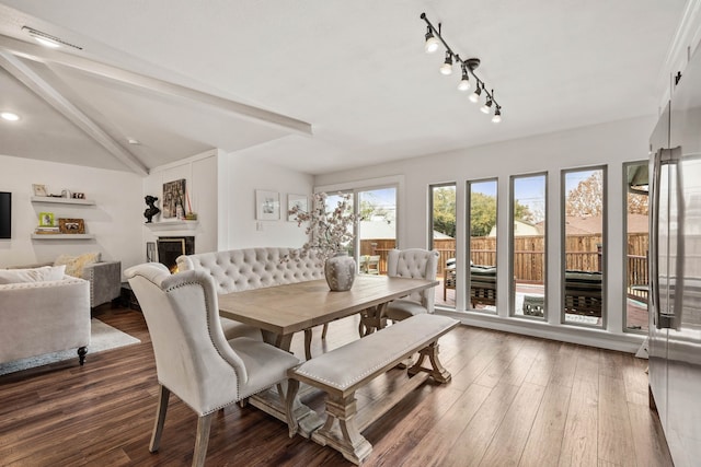 dining area with dark wood-type flooring and vaulted ceiling with beams