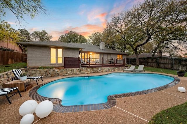 pool at dusk featuring a wooden deck and a patio