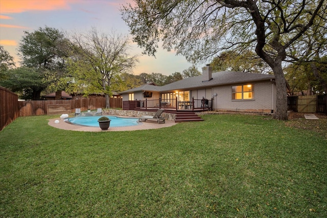 back house at dusk featuring a yard and a swimming pool side deck