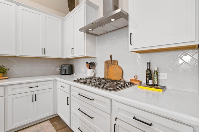 kitchen featuring dark hardwood / wood-style floors, tasteful backsplash, white cabinetry, stainless steel gas cooktop, and wall chimney range hood