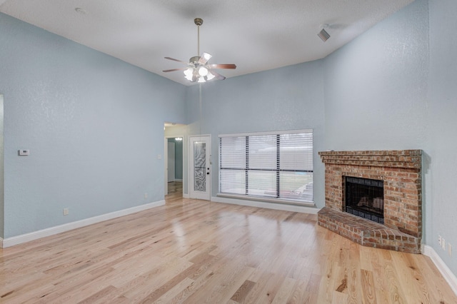 unfurnished living room with a brick fireplace, light hardwood / wood-style floors, ceiling fan, and a high ceiling