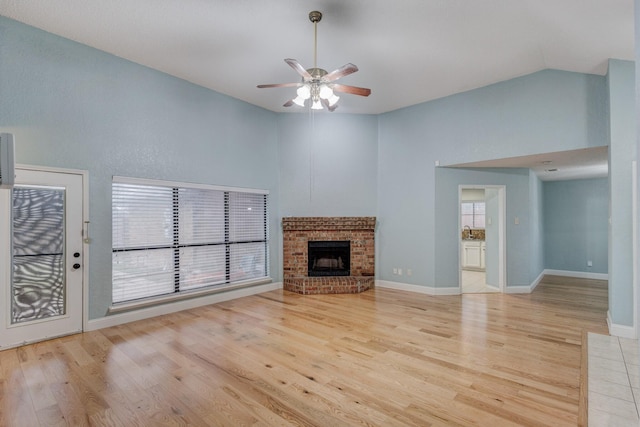 unfurnished living room with a brick fireplace, high vaulted ceiling, ceiling fan, and light hardwood / wood-style flooring