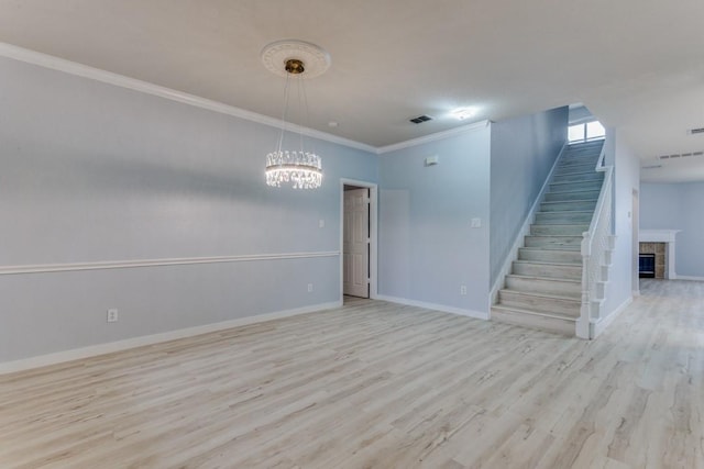 empty room featuring a notable chandelier, crown molding, a fireplace, and light hardwood / wood-style floors