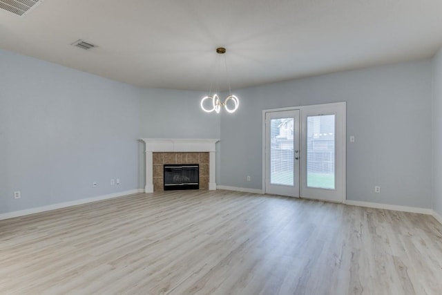 unfurnished living room featuring a tiled fireplace, a chandelier, and light wood-type flooring