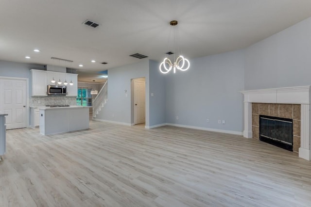 unfurnished living room with an inviting chandelier, light hardwood / wood-style flooring, and a tile fireplace