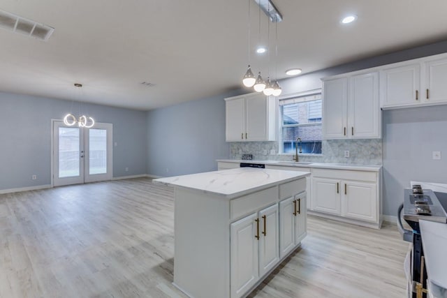 kitchen featuring sink, stainless steel stove, a center island, white cabinets, and decorative light fixtures