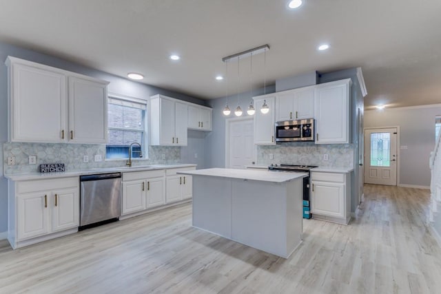 kitchen with sink, white cabinetry, stainless steel appliances, a kitchen island, and decorative light fixtures