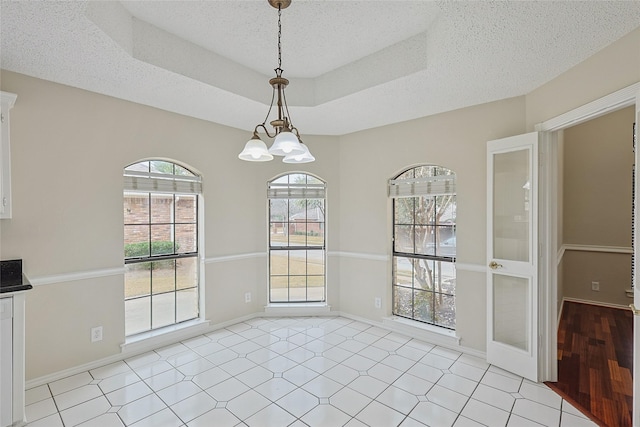 unfurnished dining area featuring a notable chandelier, a tray ceiling, and a textured ceiling