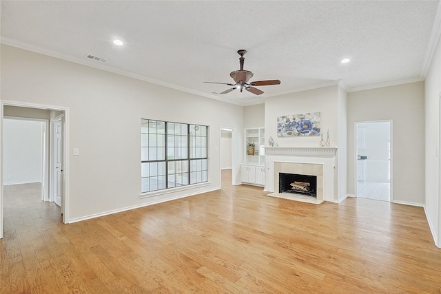 unfurnished living room with a tiled fireplace, ornamental molding, ceiling fan, a textured ceiling, and light hardwood / wood-style flooring