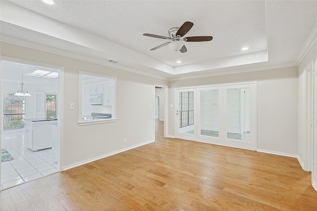 unfurnished living room with ornamental molding, a tray ceiling, light hardwood / wood-style floors, and a textured ceiling