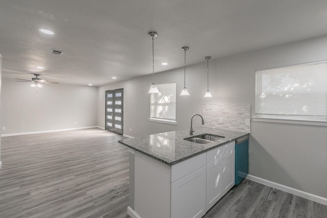 kitchen featuring sink, kitchen peninsula, stone counters, pendant lighting, and white cabinets