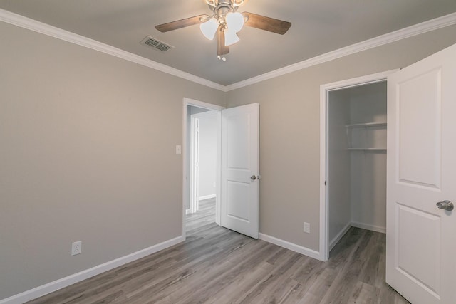 unfurnished bedroom with a walk in closet, ceiling fan, light hardwood / wood-style floors, crown molding, and a closet