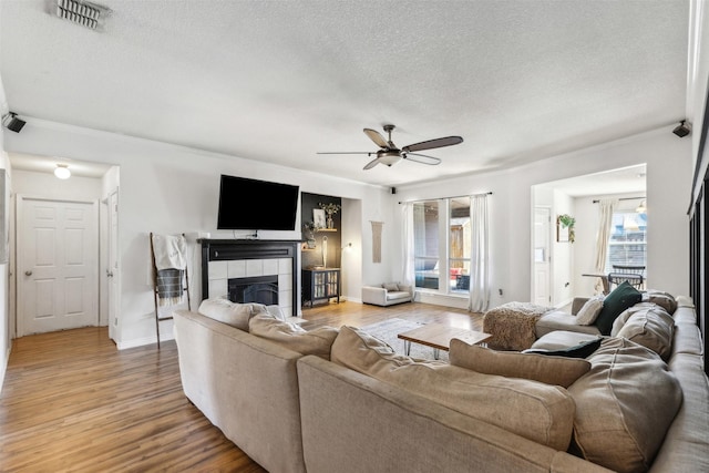 living room featuring hardwood / wood-style flooring, ceiling fan, a tile fireplace, and a textured ceiling