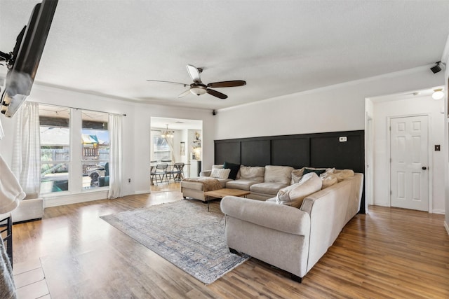 living room featuring crown molding, wood-type flooring, and ceiling fan with notable chandelier