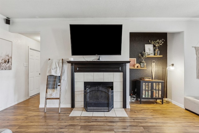 living room featuring crown molding, a fireplace, a textured ceiling, and light wood-type flooring