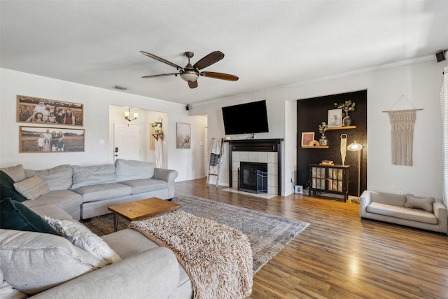 living room featuring a tiled fireplace, hardwood / wood-style flooring, ornamental molding, and ceiling fan