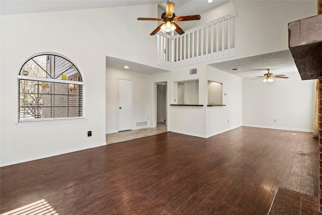 unfurnished living room featuring hardwood / wood-style flooring, ceiling fan, and a towering ceiling