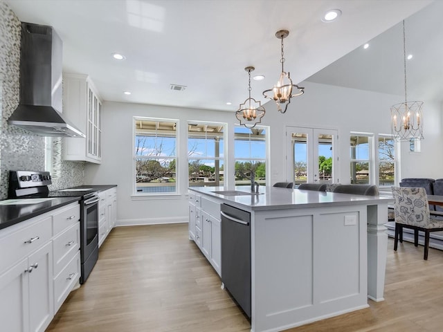 kitchen with pendant lighting, an island with sink, sink, stainless steel appliances, and wall chimney range hood