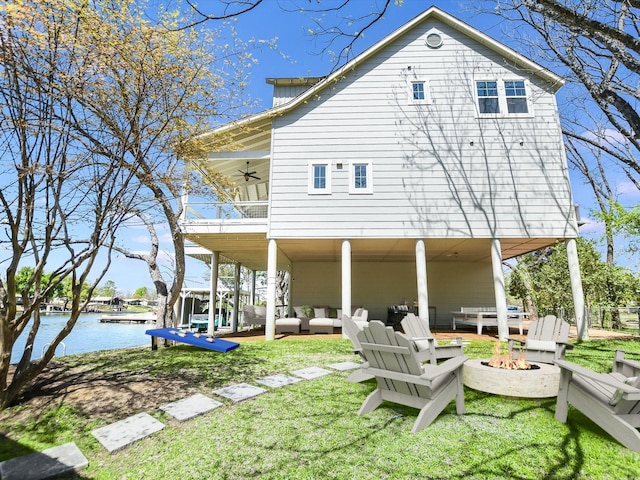 back of house with a water view, ceiling fan, a yard, and an outdoor living space with a fire pit