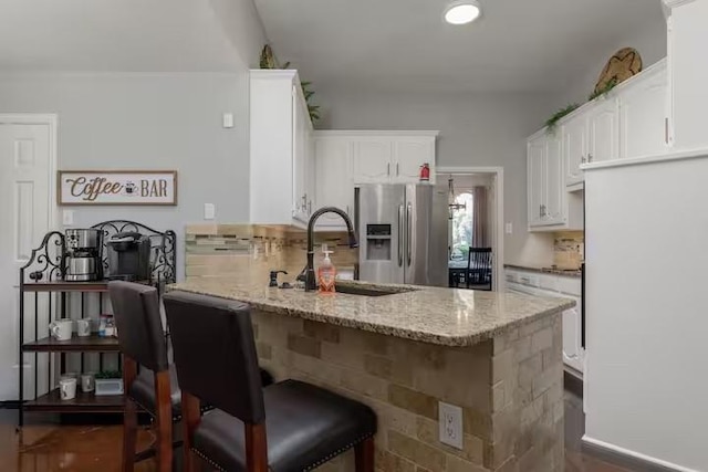 kitchen with sink, light stone counters, stainless steel fridge with ice dispenser, kitchen peninsula, and white cabinets