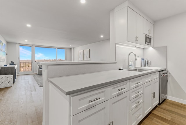 kitchen with sink, white cabinets, kitchen peninsula, stainless steel appliances, and light wood-type flooring