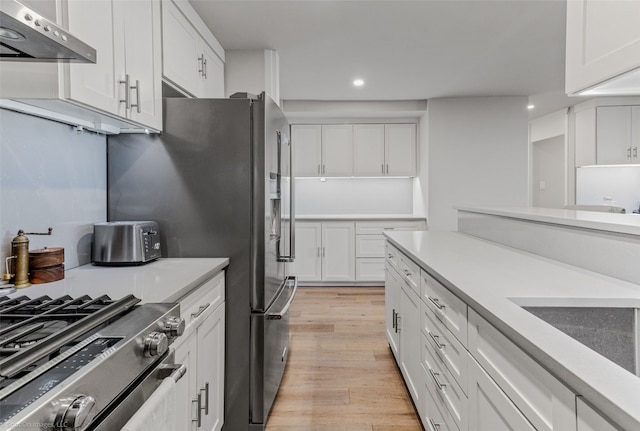 kitchen featuring stainless steel range with gas cooktop, sink, white cabinets, light wood-type flooring, and wall chimney exhaust hood