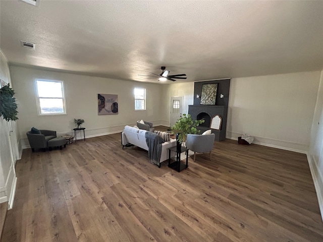 living room with a brick fireplace, dark hardwood / wood-style floors, a textured ceiling, and ceiling fan