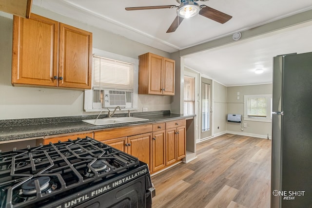 kitchen featuring heating unit, sink, stainless steel fridge, black gas stove, and light hardwood / wood-style flooring