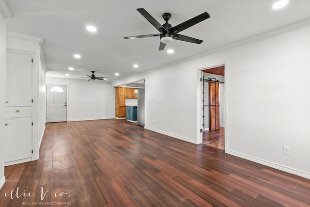 unfurnished living room featuring ornamental molding, a barn door, dark hardwood / wood-style floors, and ceiling fan