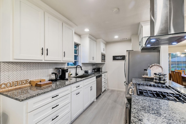 kitchen with dark stone countertops, white cabinets, stainless steel appliances, and wall chimney exhaust hood