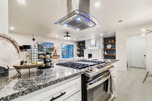 kitchen with stainless steel gas range, white cabinetry, light hardwood / wood-style flooring, dark stone countertops, and island exhaust hood