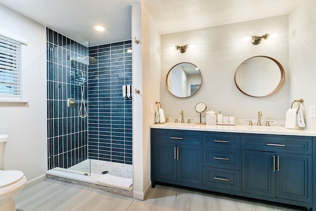 bathroom with wood-type flooring, tiled shower, vanity, and toilet