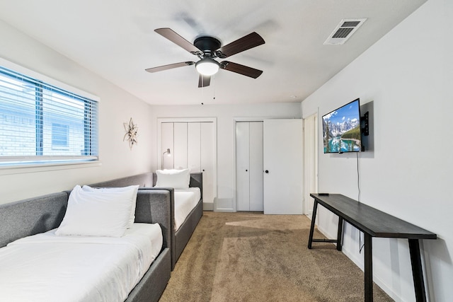 bedroom with two closets, carpet floors, and ceiling fan