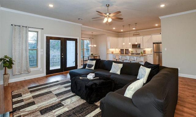 living room featuring crown molding, ceiling fan with notable chandelier, dark hardwood / wood-style floors, and french doors