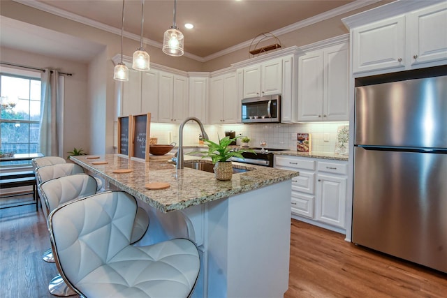 kitchen featuring white cabinetry, appliances with stainless steel finishes, an island with sink, and light stone counters