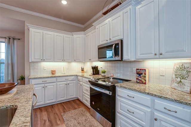 kitchen with light wood-type flooring, ornamental molding, appliances with stainless steel finishes, light stone countertops, and white cabinets