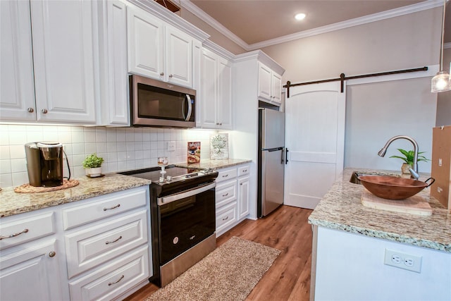 kitchen with sink, decorative light fixtures, stainless steel appliances, a barn door, and white cabinets