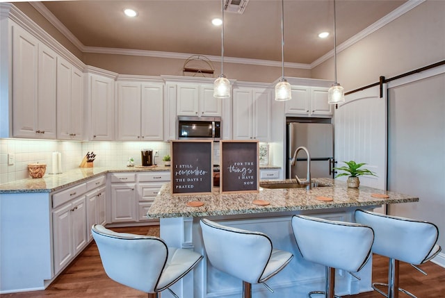 kitchen featuring decorative light fixtures, stainless steel appliances, white cabinets, and a center island with sink