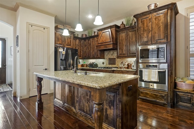 kitchen with sink, premium range hood, stainless steel appliances, light stone countertops, and a center island with sink