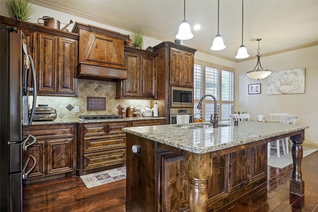 kitchen with light stone counters, stainless steel appliances, hanging light fixtures, and a center island with sink