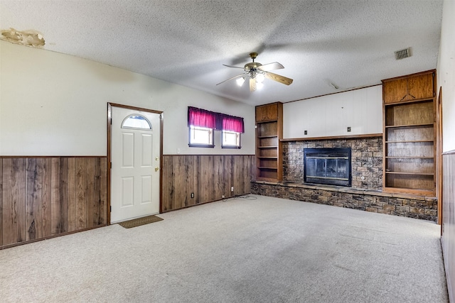 unfurnished living room with ceiling fan, a textured ceiling, a brick fireplace, light colored carpet, and wood walls