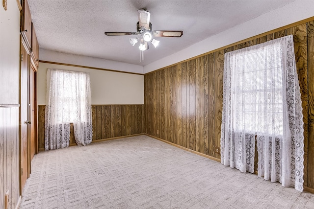 unfurnished room featuring ceiling fan, light colored carpet, a textured ceiling, and wooden walls