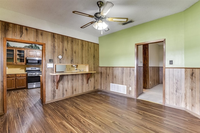 kitchen with dark hardwood / wood-style flooring, ceiling fan, kitchen peninsula, stainless steel range with gas stovetop, and a textured ceiling