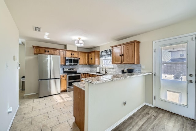 kitchen featuring tasteful backsplash, appliances with stainless steel finishes, light stone countertops, and kitchen peninsula