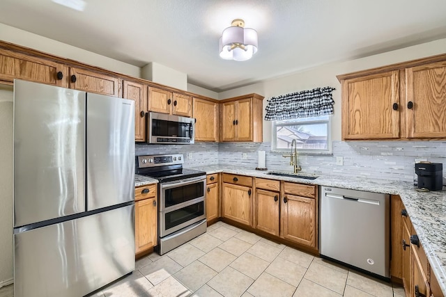 kitchen featuring sink, tasteful backsplash, light tile patterned floors, appliances with stainless steel finishes, and light stone countertops