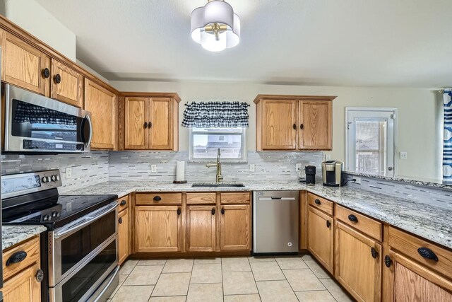 kitchen with light tile patterned flooring, sink, appliances with stainless steel finishes, light stone countertops, and decorative backsplash