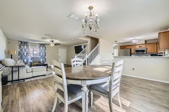 dining room with ceiling fan with notable chandelier and light wood-type flooring