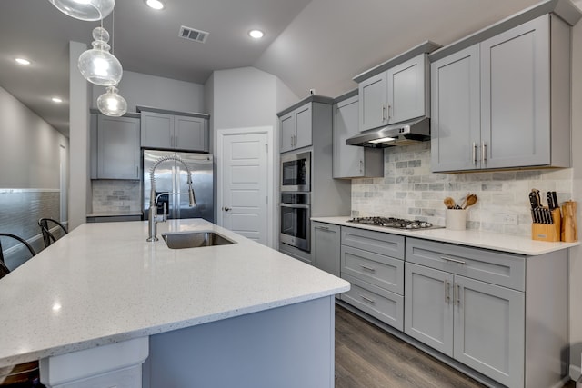 kitchen with sink, appliances with stainless steel finishes, a kitchen bar, a center island with sink, and decorative light fixtures