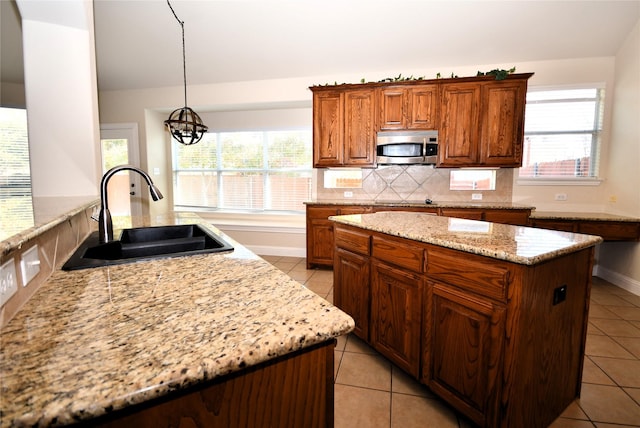 kitchen with tasteful backsplash, light stone countertops, sink, and decorative light fixtures