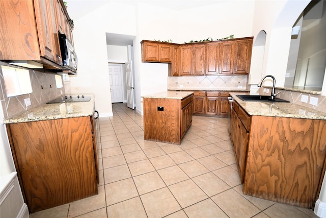 kitchen with light tile patterned flooring, sink, light stone counters, a center island, and decorative backsplash